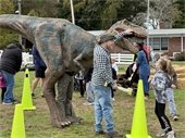 Kids jump up to touch a dinosaur with the dinosaur keeper's help